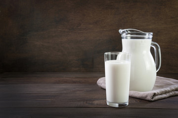 Fresh milk in glass and pitcher on dark wooden table. Rustic style.