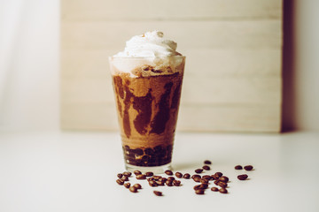 Ice coffee in the glass topped whipping cream with coffee beans. Cold summer drink on wooden background and copy space. Advertising for caramel mocha and chocolate beverage for the cafe.