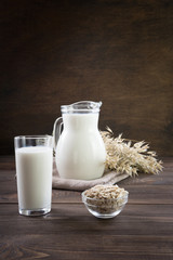 Fresh oat milk in glass and pitcher on dark wooden table. Rustic style.