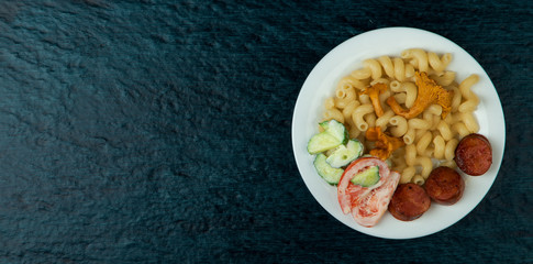 FOOD IN POT. PASTA, SALAD AND FOX MUSHROOMS IN THE WHITE CERAMIC PLATE ON A DARK BACKGROUND. VIEW FROM ABOVE. COPY SPACE