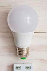 LED light bulb and remote control with buttons on and off on a white wooden background