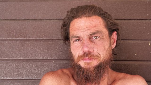 Down-and-out person on the street. Homeless man looks at the camera. Real person with no fixed abode