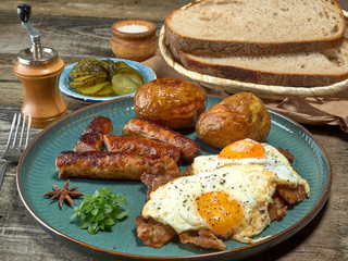 Fried sausages with potatoes,scrambled eggs and bacon.On wooden background