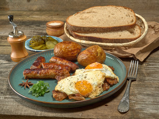 Fried sausages with potatoes,scrambled eggs and bacon.On wooden background