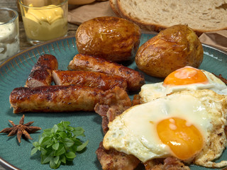 Fried sausages with potatoes,scrambled eggs and bacon.On wooden background