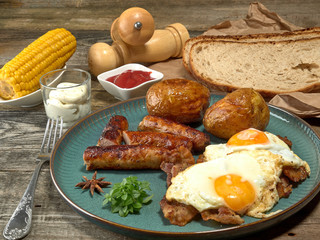 Fried sausages with potatoes,scrambled eggs and bacon.On wooden background