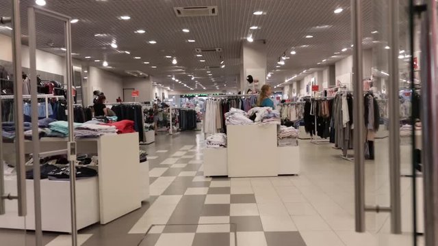 Young attractive woman at a clothing store in a mall looks at clothes for trying on and shopping. She picks up fashionable clothes. Shopping at the mall or airport shops.
