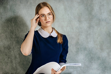 Dramatic portrait of a beautiful lonely girl with blond hair, isolated on a gray background in a studio shot, with a notebook in her hands, Belarus