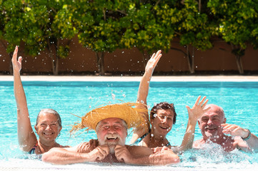 Four senior people friends laughing enjoying the swimming pool together. Bright sunlight and transparent water. Large smiles and happiness. Floating in the water