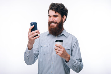 Photo of excited man using his smartphone and holding cup of coffee