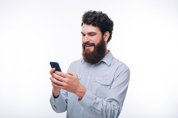 Young smiling hipster bearded man in casul using his phone over white background