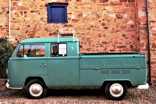Camioneta o furgoneta vintage de los años 60 de color verde, delante de un muro de piedra de un pueblo de España