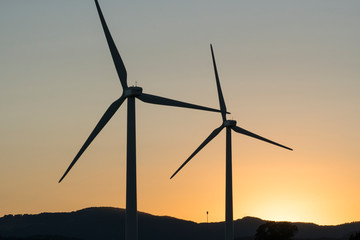 Wind turbines, green energy windmills silhouetted against golden sunset sky, Northern California...