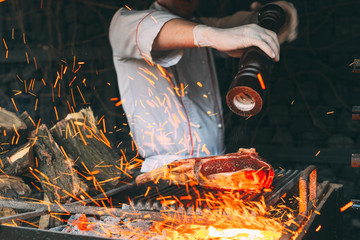 Chef pepper the steak on fire. - obrazy, fototapety, plakaty