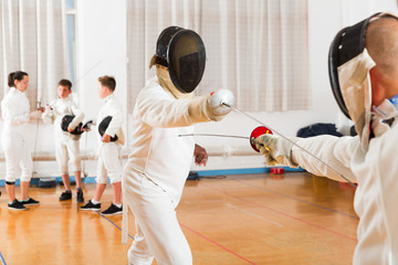 Adults and teens wearing fencing uniform practicing with foil