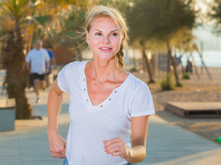 Smiling adult woman in white T-shirt is jogging in the park