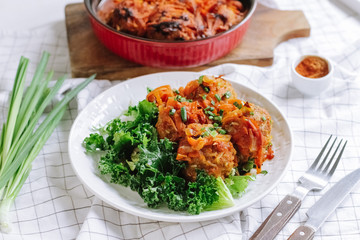white bowl of home cooked meatballs with vegetables and salad leaves.