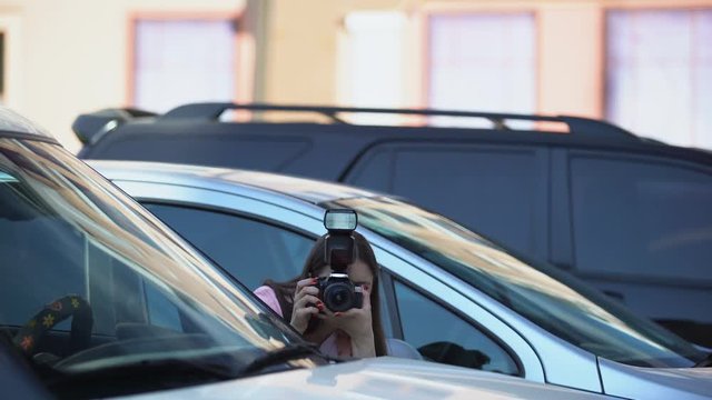 Female yellow press journalist hiding in parking lot, taking photos, sensation