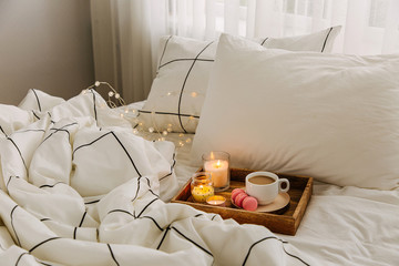 Wooden tray of coffee and candles on bed. White bedding sheets with striped blanket and pillow....