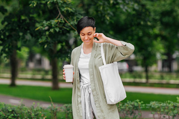 Woman with short hair holding reusable coffee cup and eco bag enjoying morning. Eco friendly concept.