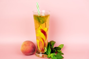 Refreshing summer cold tea on pink background. Ice tea with peach and mint leaves.