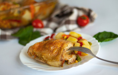 Bits of the roasted chicken with vegetables on the white plate and light background. Сhicken thighs with pepper, baby carrot, green beans and spice. Healthy quick lunch or a dinner for family