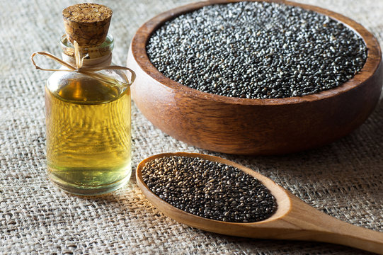 Glass bottle of chia oil and Chia seeds ( Salvia Hispanica ) in wooden spoon and bowl on burlap sack backdrop. Cereal healthy food contains omega 3, a dietary supplement gluten free
