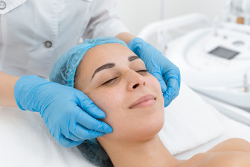 Beautician makes professional massage of the patient's face. A young girl is undergoing a course of spa treatments in the office of a beautician. Moisturizing, cleaning and facial skin care. Cosmetic 