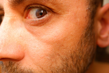 A man looks sideways at the camera at a strange and suspicious angle, with his eye wide open.