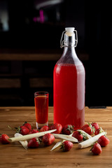 Bottle of sweet strawberry liqueur on a bar counter on wooden table with blurred background