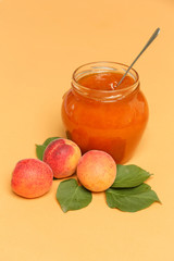 Jar of apricots jam and fresh apricots on an orange background	