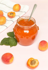 Fototapeta na wymiar Jar of apricots jam and fresh apricots on pink background 