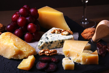 Assorted cheeses, nuts, grapes, fruits, smoked meat and a glass of wine on a serving table. Dark and Moody style. Free space for text.