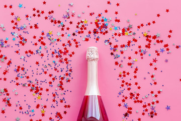 Party with champagne bottle and colorful party streamers on pink background top view pattern