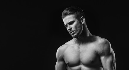 Naklejka premium Black and white. Muscular model sports young man on dark background. Fashion portrait of strong brutal guy with a modern trendy hairstyle. Sexy torso. Male flexing his muscles.