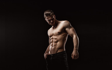 Fototapeta na wymiar Muscular model sports young man on dark background. Fashion portrait of strong brutal guy with a modern trendy hairstyle. Sexy torso. Male flexing his muscles.