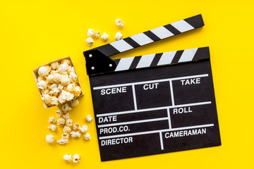 Movie premiere concept with clapperboard, popcorn on yellow background top view
