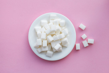 white plate full of sugar cubes on pink background, risk of diabetes, flat layout, top view