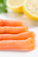 Smoked salmon slices with lemon halves on white plate (Selective Focus, Focus on the first slice)