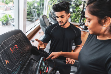 Well qualified trainer explains to his client how to use treadmill, wearing black t shirt and red...