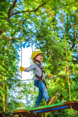 Naklejka na ściany i meble Kids boy adventure and travel. High ropes walk. Playground. Hike and kids concept. Climber child on training. Cute school child boy enjoying a sunny day in a climbing adventure activity park.
