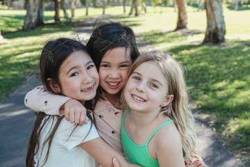 Happy and healthy mixed ethnic young little girls hugging and smiling in the park, best friends and...