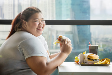 Happy fat woman eats a hamburger in restaurant