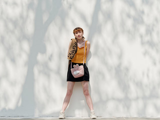 Portrait of happy Chinese girl in yellow halter top and short skirt posing on sunny street with...
