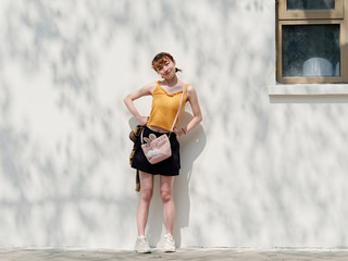 Portrait of happy Chinese girl in yellow halter top and short skirt posing on sunny street with...