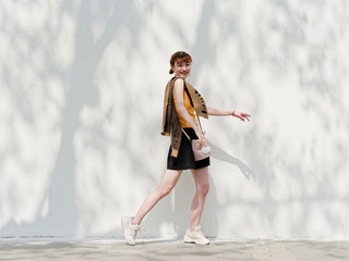 Portrait of happy Chinese girl in yellow halter top and short skirt posing on sunny street with...