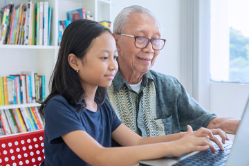 Little girl learns to use a laptop with her grandfather