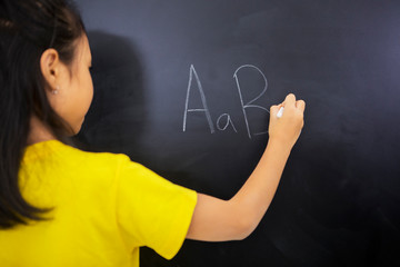 Little girl writing alphabet letters on the blackboard