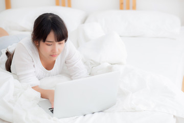 Obraz na płótnie Canvas Beautiful portrait asian young woman smile lying on bed using laptop computer with happy at bedroom for leisure and relax, freelance with girl working notebook, communication concept.