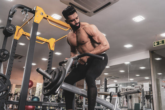 Muscular men exercising with weights. He is performing T bar rows for back muscle / Bodybuilder in the gym
